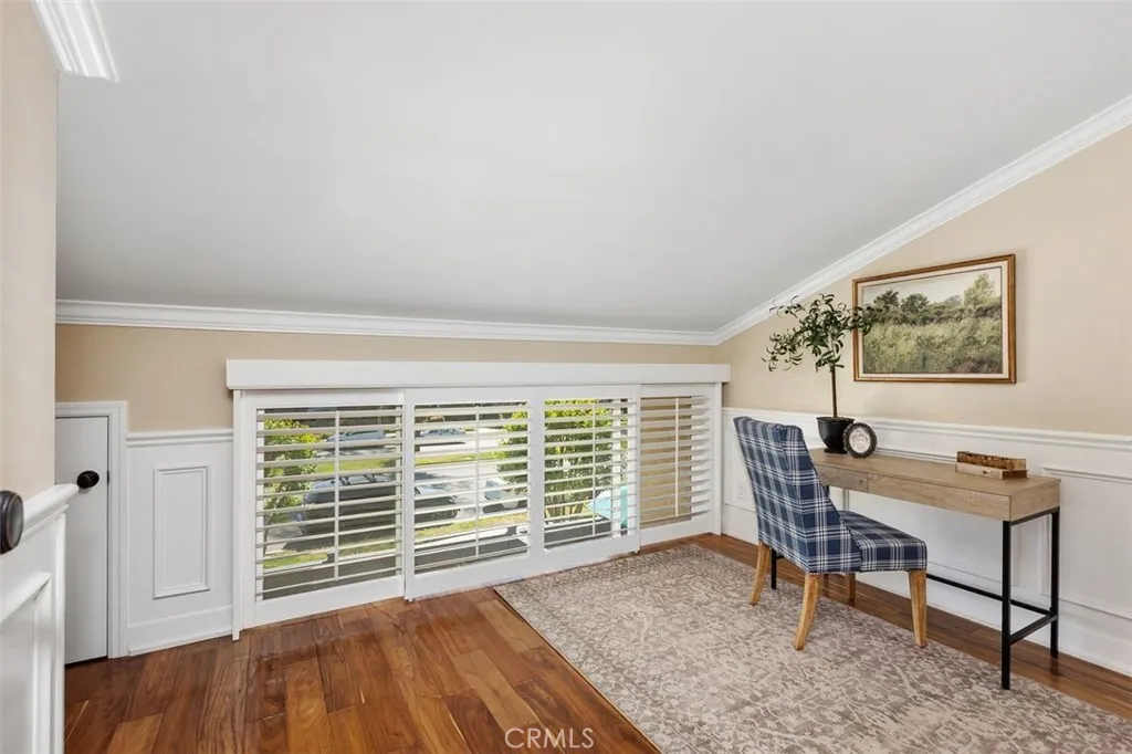 Office or Den – Light-filled bedroom with large window, neutral walls, and warm wood-look flooring.
