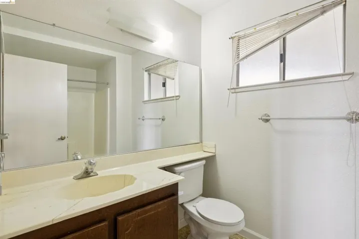 Bathroom featuring a vanity with a light-toned countertop and integrated sink, a dark wood-finish cabinet, a large wall-mounted mirror, and a toilet