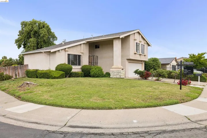 Stucco exterior residence featuring a front-facing garage, mature landscaping, and an established lawn