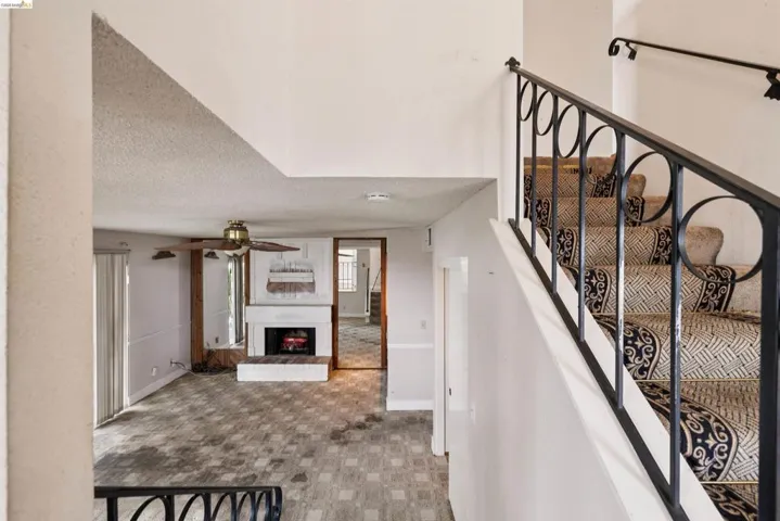 Staircase with ornamental metal railing, a prominent fireplace, and an overhead ceiling fan