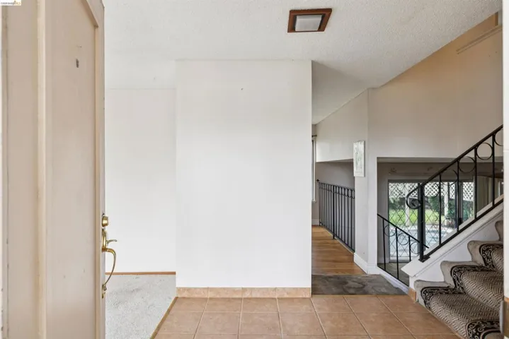 Entry foyer featuring tile flooring, a carpeted staircase with an ornate wrought iron railing, and a wood-finish hallway with a matching wrought iron railing