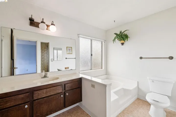 Bathroom featuring a built-in vanity with dark wood cabinetry and an integrated sink, a large wall-mounted mirror, a privacy window, a built-in tub, and a white toilet
