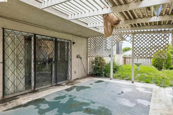 Expansive concrete patio area with an overhead pergola structure, leading to a lawn space