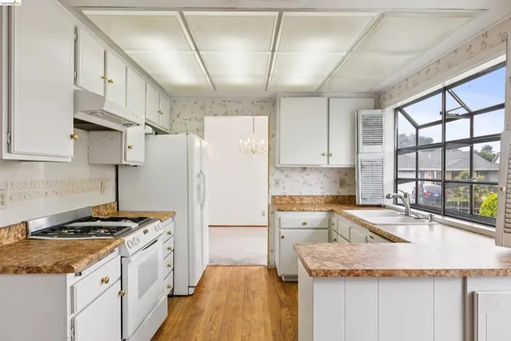 Well-lit kitchen featuring wood-finish flooring, white cabinetry with gold-tone hardware, and a gas range