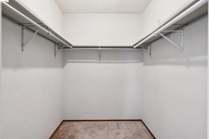 Walk-in closet featuring white walls, textured ceiling, and a built-in shelving system with hanging rods