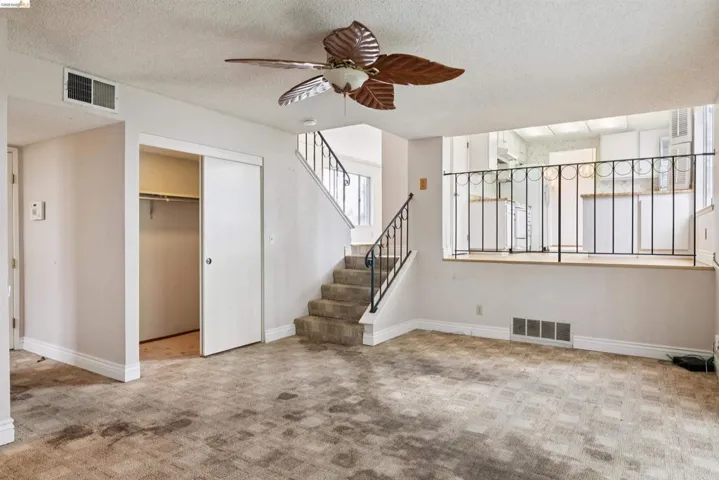 Living area featuring a ceiling fan, staircase with metal railing, and a pass-through opening to the kitchen