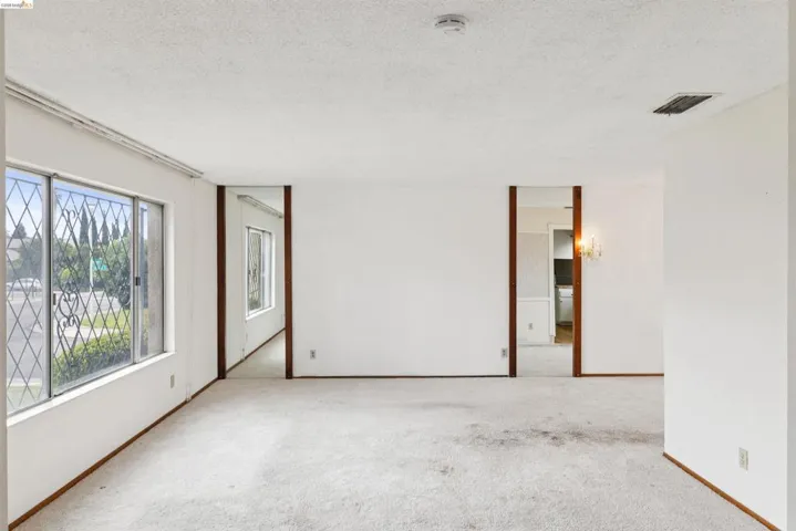 Spacious room featuring multiple large windows with security bars, white textured ceilings, and light-colored carpeting