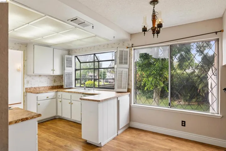 Kitchen featuring white cabinetry, wood-finish flooring, and a large window overlooking exterior greenery