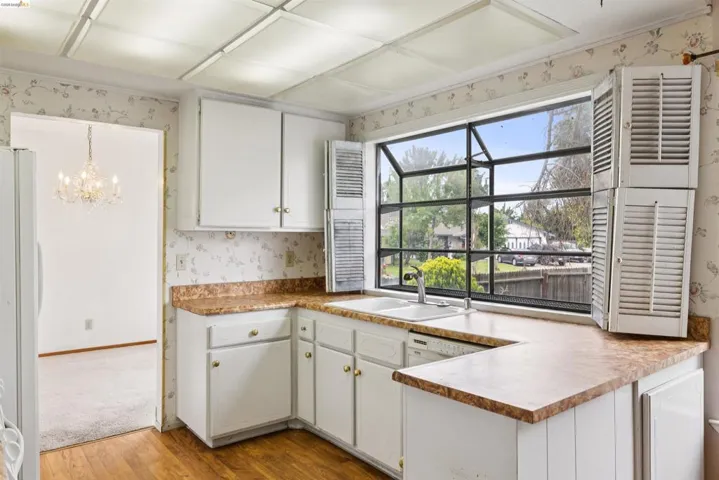 Kitchen featuring a U-shaped countertop, white cabinetry with brass-toned hardware, a double basin sink, and a large multi-pane window