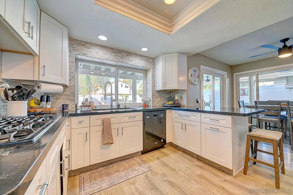Every detail considered. Gas cooktop, granite countertops, white shaker cabinetry, stacked stone accent wall, tray ceiling with recessed lighting, and a pool-view window over the sink. This kitchen was designed to impress and built to perform.