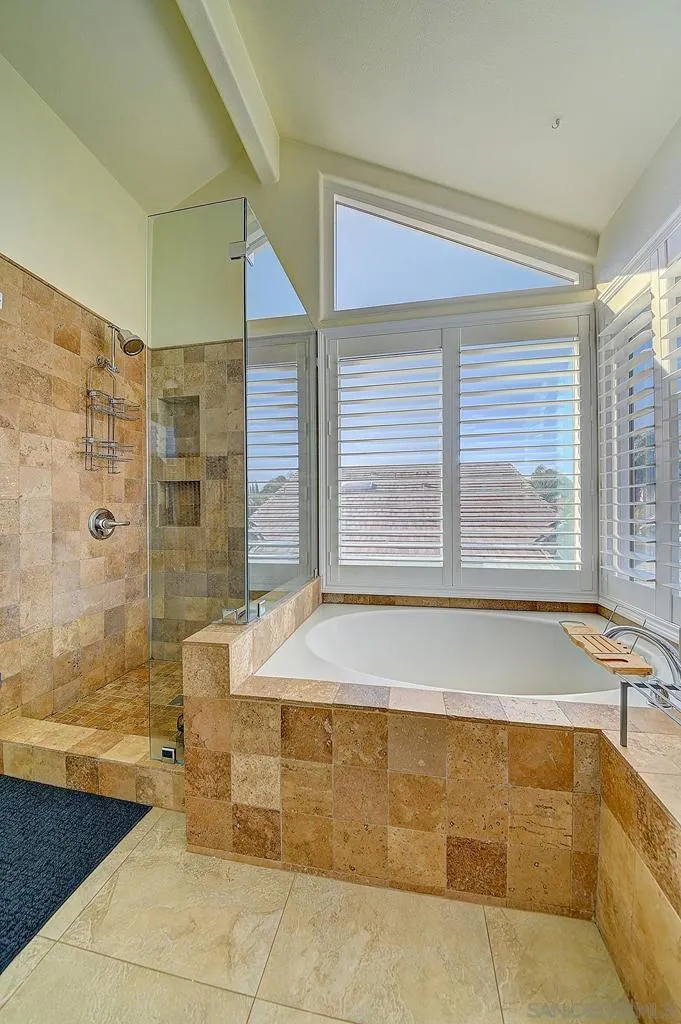 Spa-quality finishes at home. Travertine-surround soaking tub bathed in natural light, glass-enclosed walk-in shower with built-in niches, and vaulted ceilings — this en suite is a daily retreat, not just a bathroom.