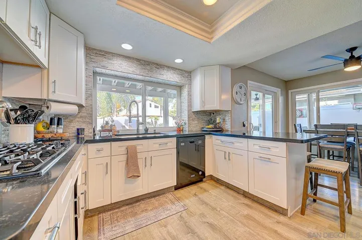 Every detail considered. Gas cooktop, granite countertops, white shaker cabinetry, stacked stone accent wall, tray ceiling with recessed lighting, and a pool-view window over the sink. This kitchen was designed to impress and built to perform.