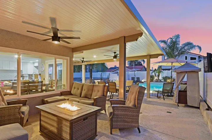 Southern California evenings were made for this. Alumawood patio cover with ceiling fans, crackling fire pit lounge, wicker seating, outdoor TV, and pool views glowing at dusk — your outdoor living room is open 365 days a year.