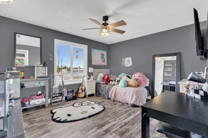 Spacious room featuring wood-finish flooring, a ceiling fan with integrated lighting, and a large window with horizontal blinds