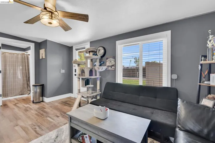 Living space featuring wood-finish flooring, a ceiling fan with integrated lighting, and neutral grey walls