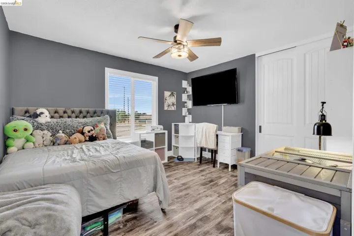 Interior room featuring wood-finish flooring, a white-framed window with blinds, and a ceiling fan with light fixture