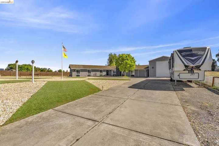 Spacious concrete driveway with a gravel border leading to a detached garage and a gray-sided residence