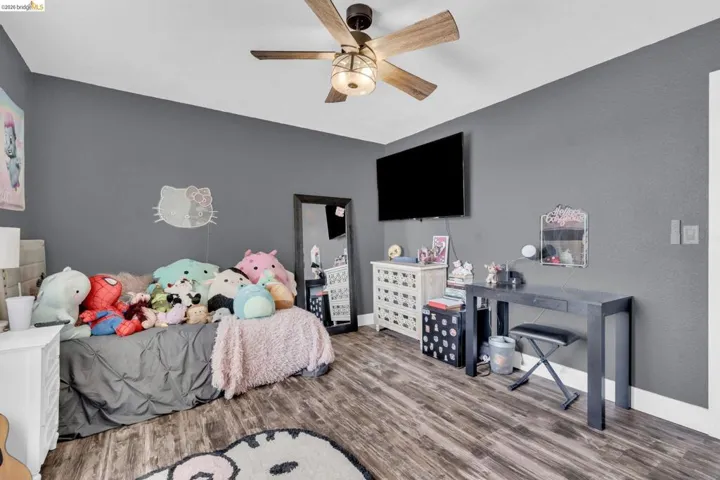 Room featuring wood-finish flooring, a ceiling fan with integrated lighting, a wall-mounted display, and gray painted walls
