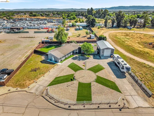 Expansive property featuring a single-story residence, a large detached garage/shop, and a circular gravel driveway with integrated lawn sections