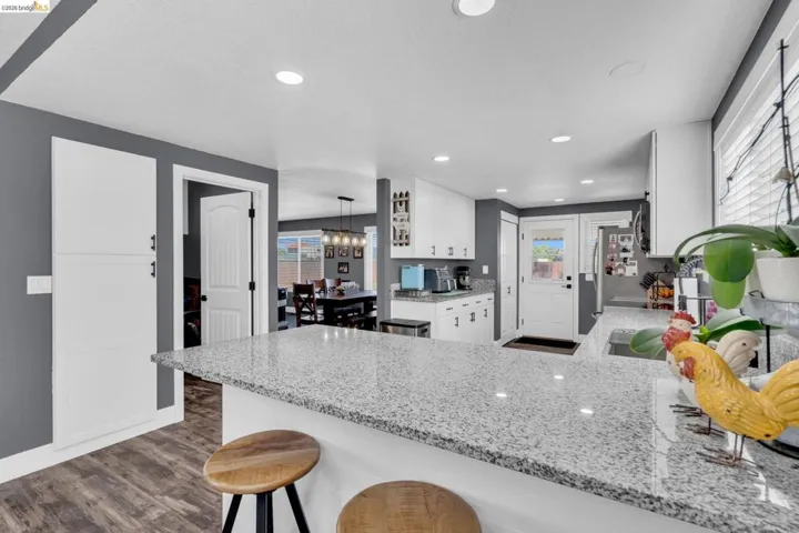 Kitchen featuring a spacious island with a speckled countertop, white cabinetry, recessed lighting, and wood-finish flooring