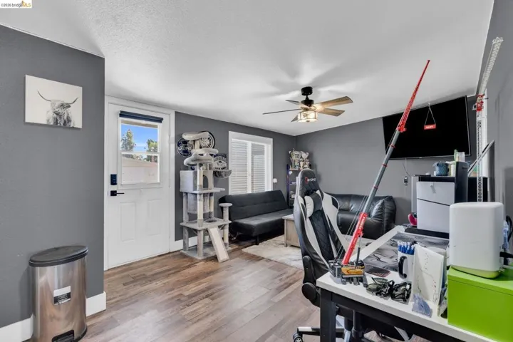 Spacious interior room featuring wood-finish flooring, a ceiling fan with integrated lighting, and a white paneled door with an upper window