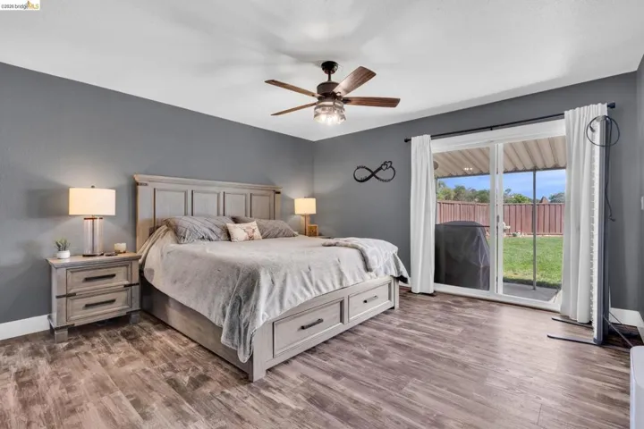 Spacious room featuring wood-finish flooring, a ceiling fan with integrated lighting, and a sliding glass door providing direct access to the exterior patio and fenced yard