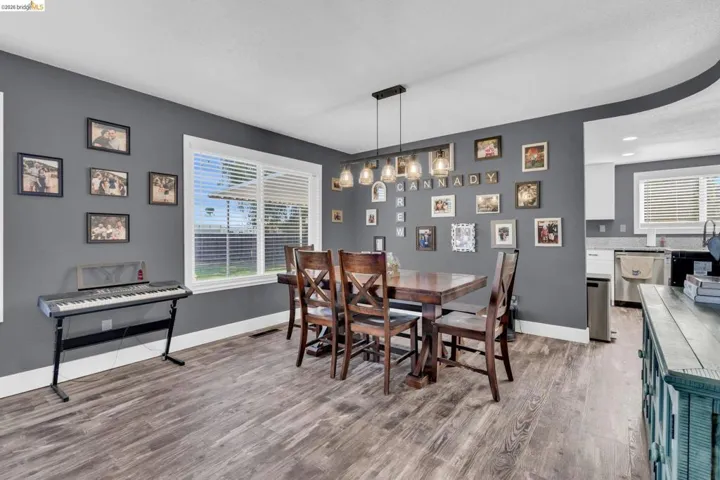 Spacious dining area featuring wood-finish flooring, a large window with blinds, and a linear pendant light fixture