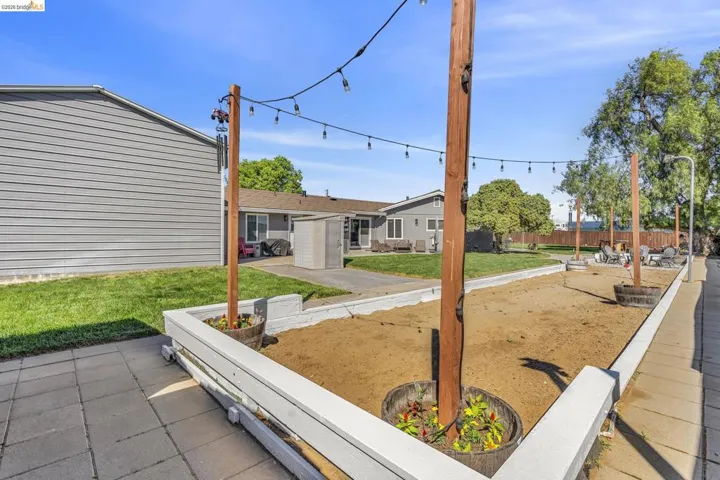 Spacious outdoor area featuring a sand-filled court, string lighting, and low white perimeter walls