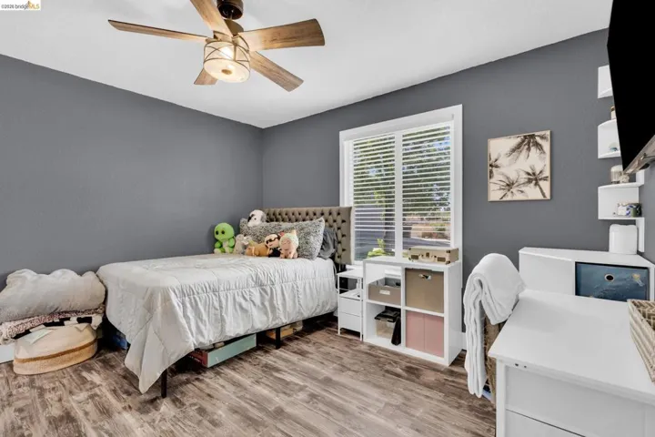 Room featuring wood-finish flooring, a ceiling fan with integrated lighting, and a window with horizontal blinds