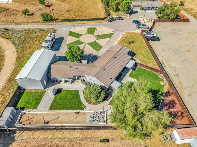 Expansive property featuring a large metal barn, paved driveways, a circular artificial turf design, established trees, and a fenced perimeter