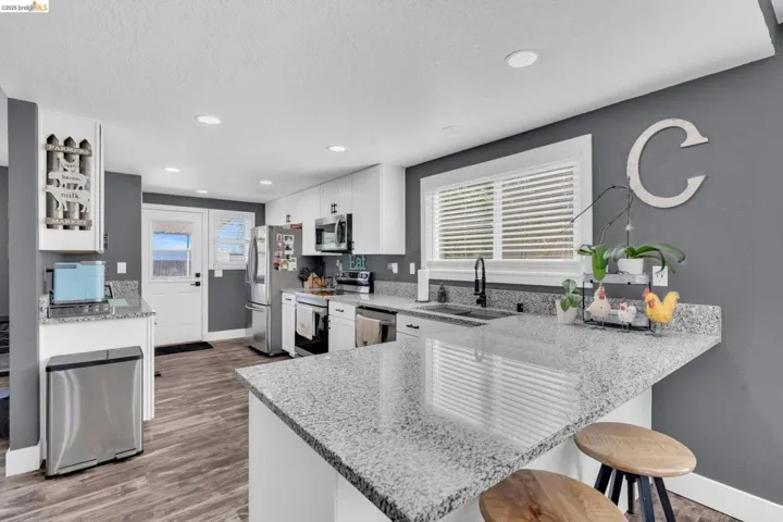 Modern kitchen featuring wood-finish flooring, white cabinetry, recessed lighting, and granite countertops