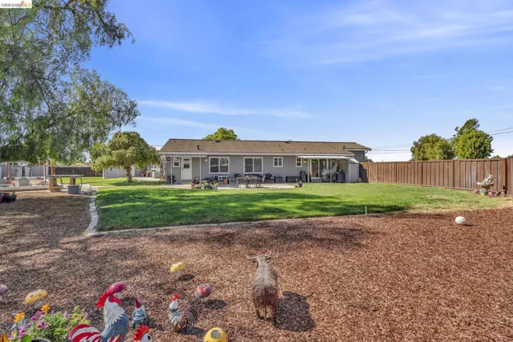 Expansive backyard featuring a manicured lawn, wood chip landscaping, a full privacy fence, and mature trees