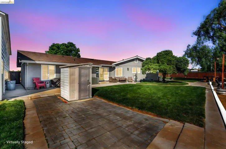 Expansive backyard featuring a manicured lawn, established shade trees, and a paved patio area