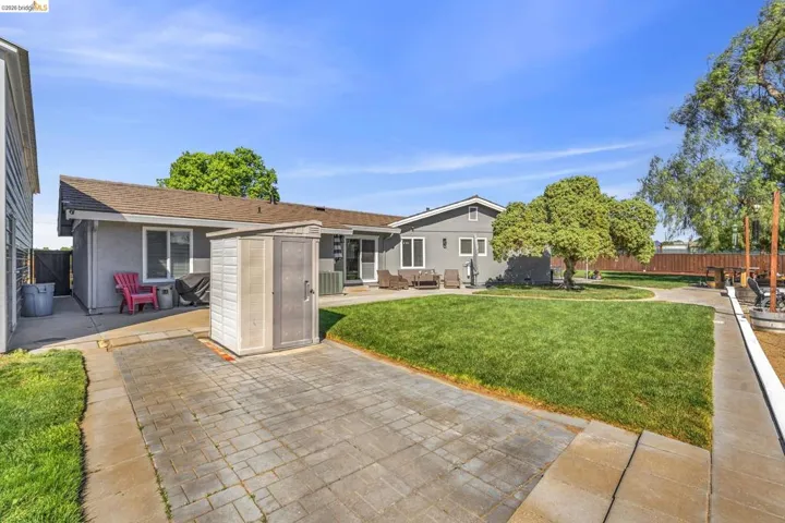 Expansive outdoor space featuring a large manicured lawn, paver patio, mature trees, and a storage shed