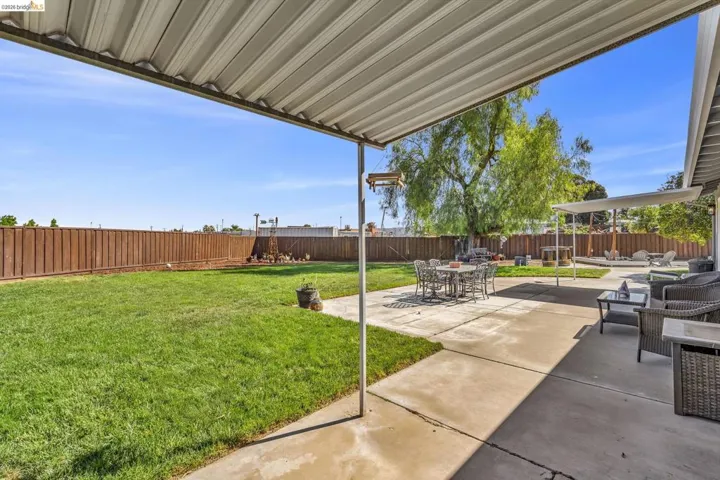 Expansive backyard featuring a covered patio, concrete paving, a large manicured lawn, and a perimeter privacy fence