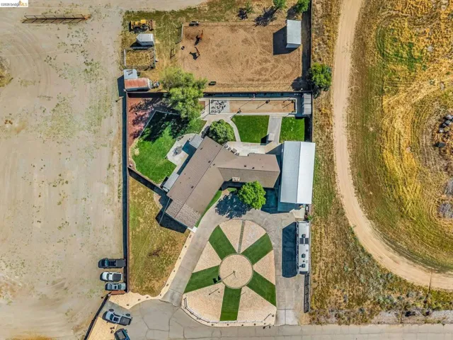 Expansive property featuring a circular driveway with integrated landscaping, a large main residence, a detached metal structure, multiple outbuildings, and a fenced pasture area