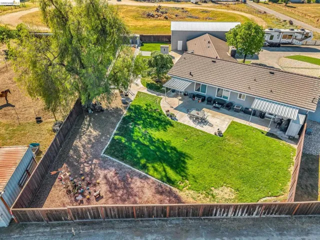 Spacious backyard featuring a manicured lawn area, expansive concrete patio, and mature shade trees