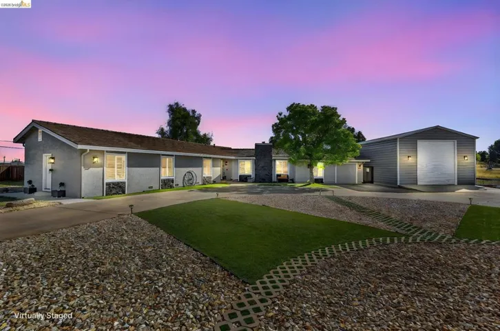 Exterior featuring a gravel driveway, artificial turf accents, and a detached metal building with a roll-up door