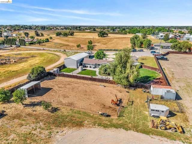 Expansive property featuring a large main residence, a substantial metal-sided outbuilding, a fenced backyard with mature trees, and additional open land with a covered structure