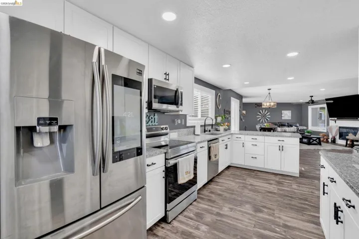 Modern kitchen featuring stainless steel appliances, white cabinetry, granite countertops, wood-finish flooring, and recessed lighting