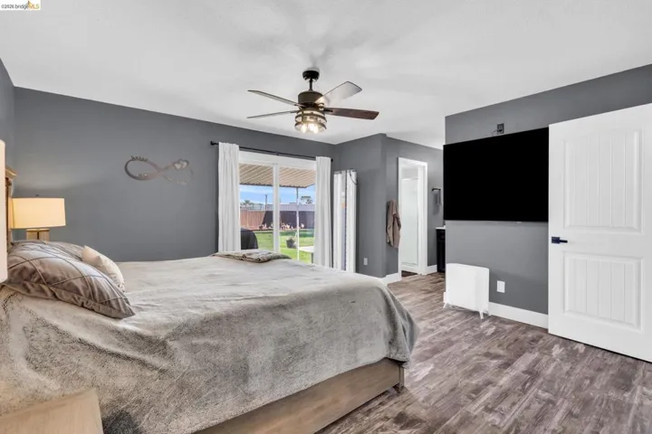 Bedroom featuring wood-finish flooring, a ceiling fan with integrated lighting, and a sliding glass door providing direct access to the backyard
