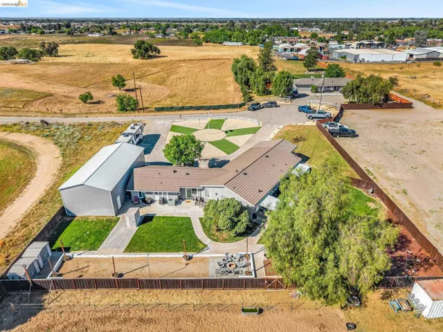 Spacious property featuring a large metal outbuilding, expansive paved driveway, dedicated parking area, fenced perimeter, and a fire pit area