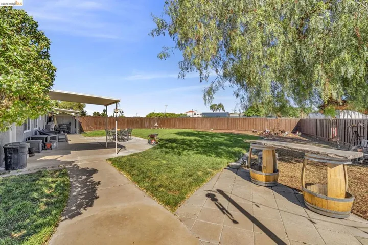 Expansive backyard featuring a manicured lawn, concrete patio, and a covered patio area