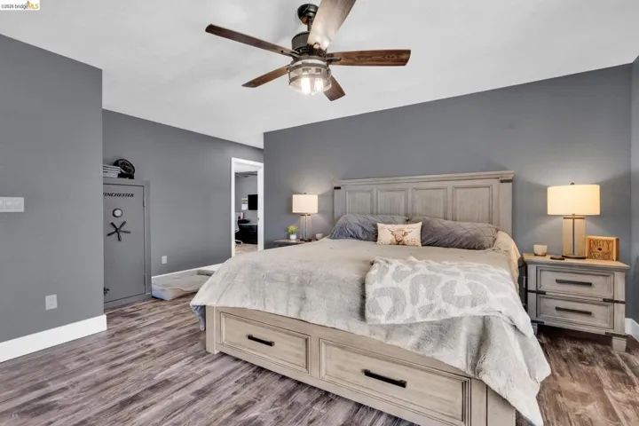 Spacious bedroom featuring wood-finish flooring, a ceiling fan with integrated lighting, and a neutral gray wall palette