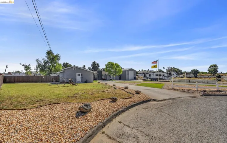 Spacious property featuring a gravel-lined driveway, manicured lawn, and a light-grey detached building