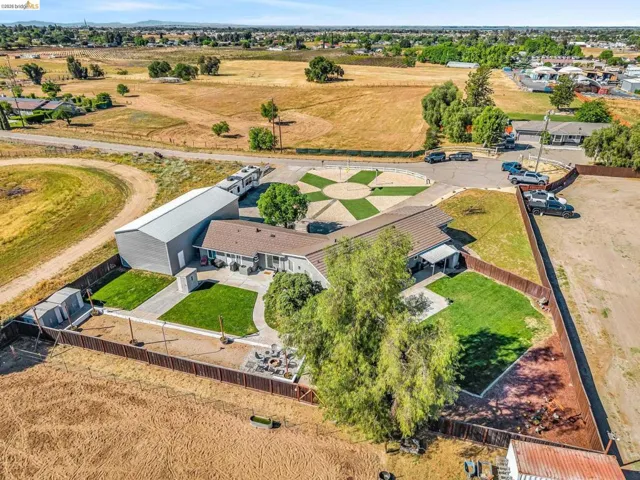 Expansive property featuring a large metal outbuilding, manicured lawns, a circular paved driveway with a geometric turf inlay, a covered patio, and a dedicated fire pit area