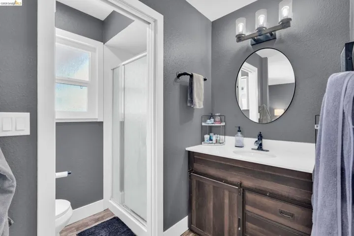 Bathroom featuring a wood-finish vanity with a white countertop, an oval mirror, and a three-light vanity fixture