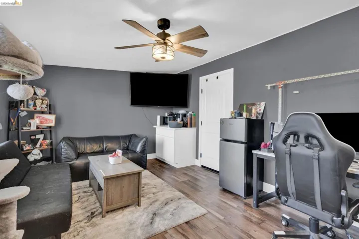 Spacious room featuring wood-finish flooring, a ceiling fan with integrated lighting, and a white paneled door