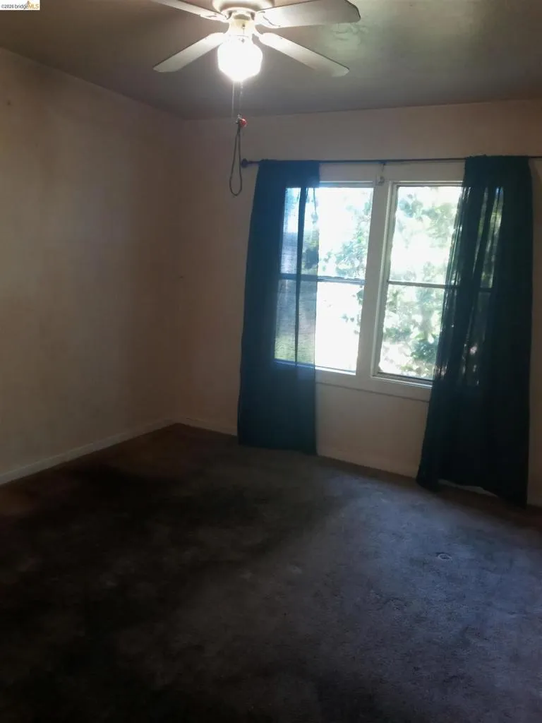 Room featuring a window with dark drapes, a ceiling fan with light fixture, and dark carpet flooring