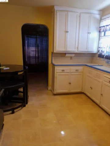 Kitchen area featuring white cabinetry with silver-tone hardware, a light-toned countertop, and tan tile flooring